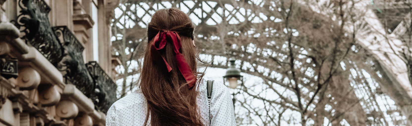 Eine Frau mit roter Schleife im Haar steht mit dem Rücken zur Kamera nah am Eifelturm